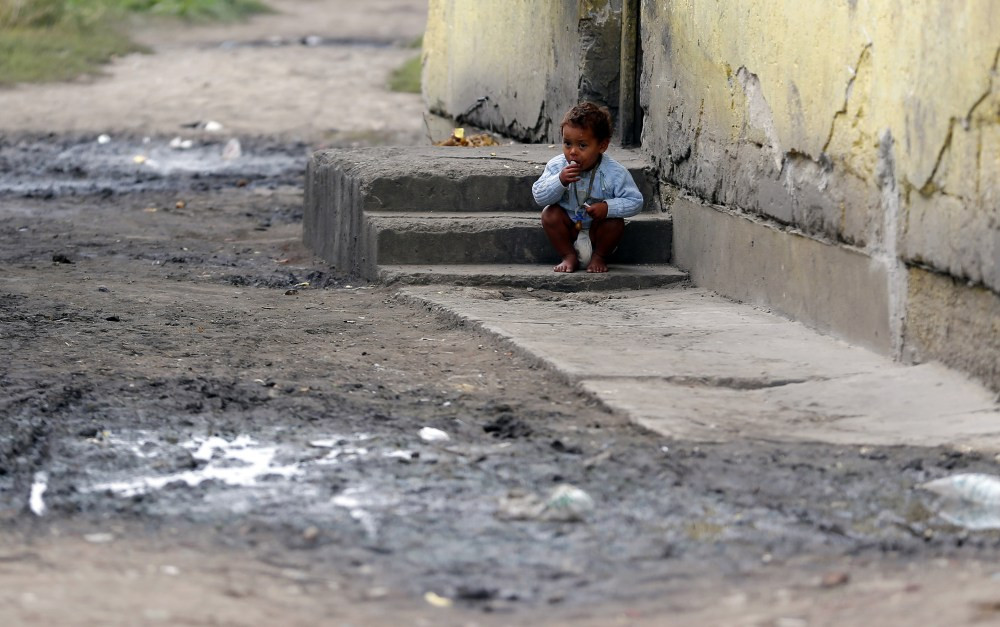 Roma baby squats on a step in a slum in Tiszavasvari